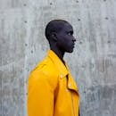 A fashion-forward portrait of a man in a vibrant yellow jacket against a concrete backdrop.